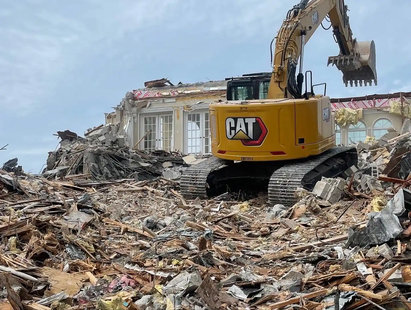 Excavator standing on a large debris pile beside a partly demolished building