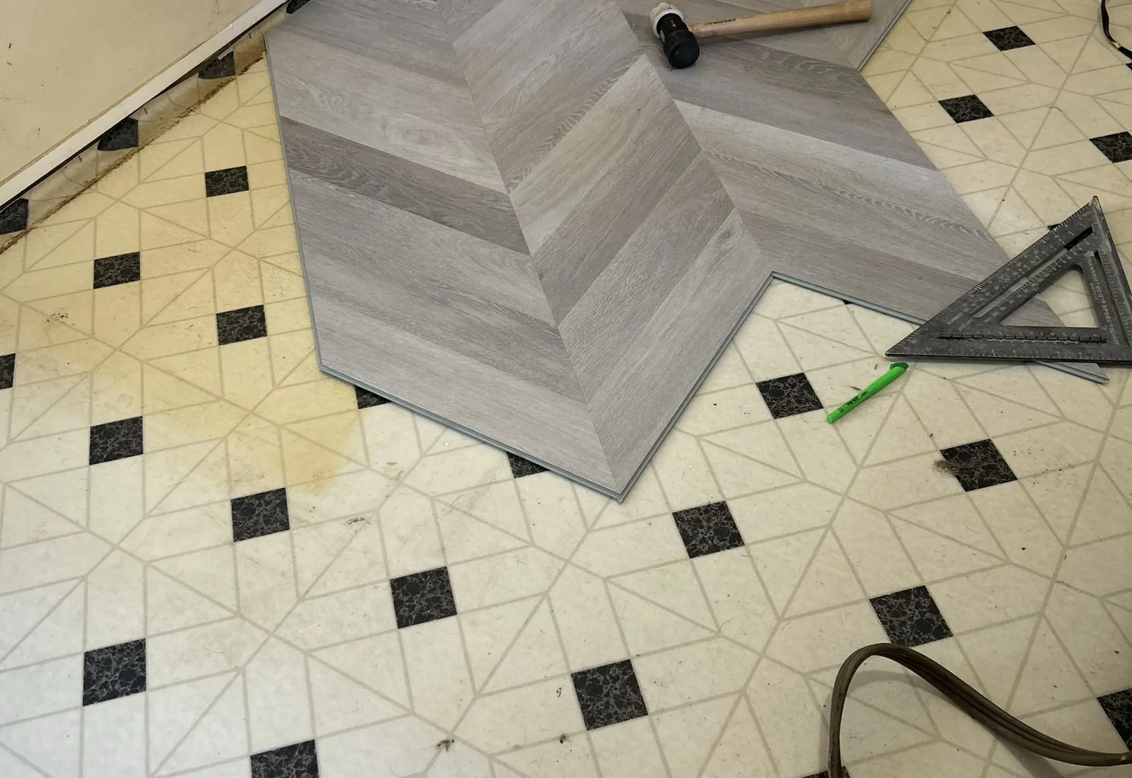 Chevron vinyl plank flooring being laid over an old vinyl tile kitchen floor with a mallet and square